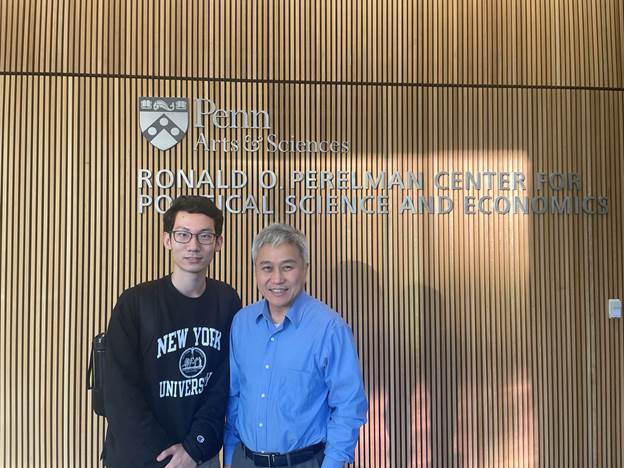 Two men standing in front of a signDescription automatically generated with medium confidence